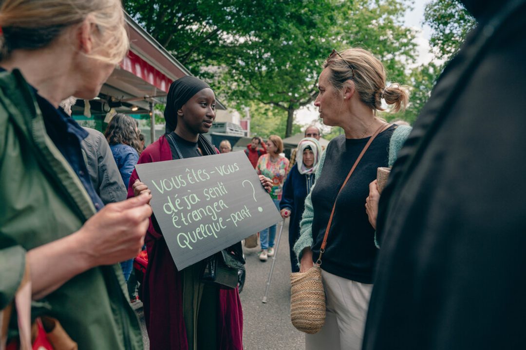 Une femme tient une pancarte posant la question suivante : « Vous êtes-vous déjà senti étranger quelque part ? »